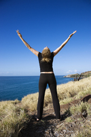 Back view of Caucasian mid-adult woman standing on Maui, Hawaii coast with arms outstretched and head thrown back.